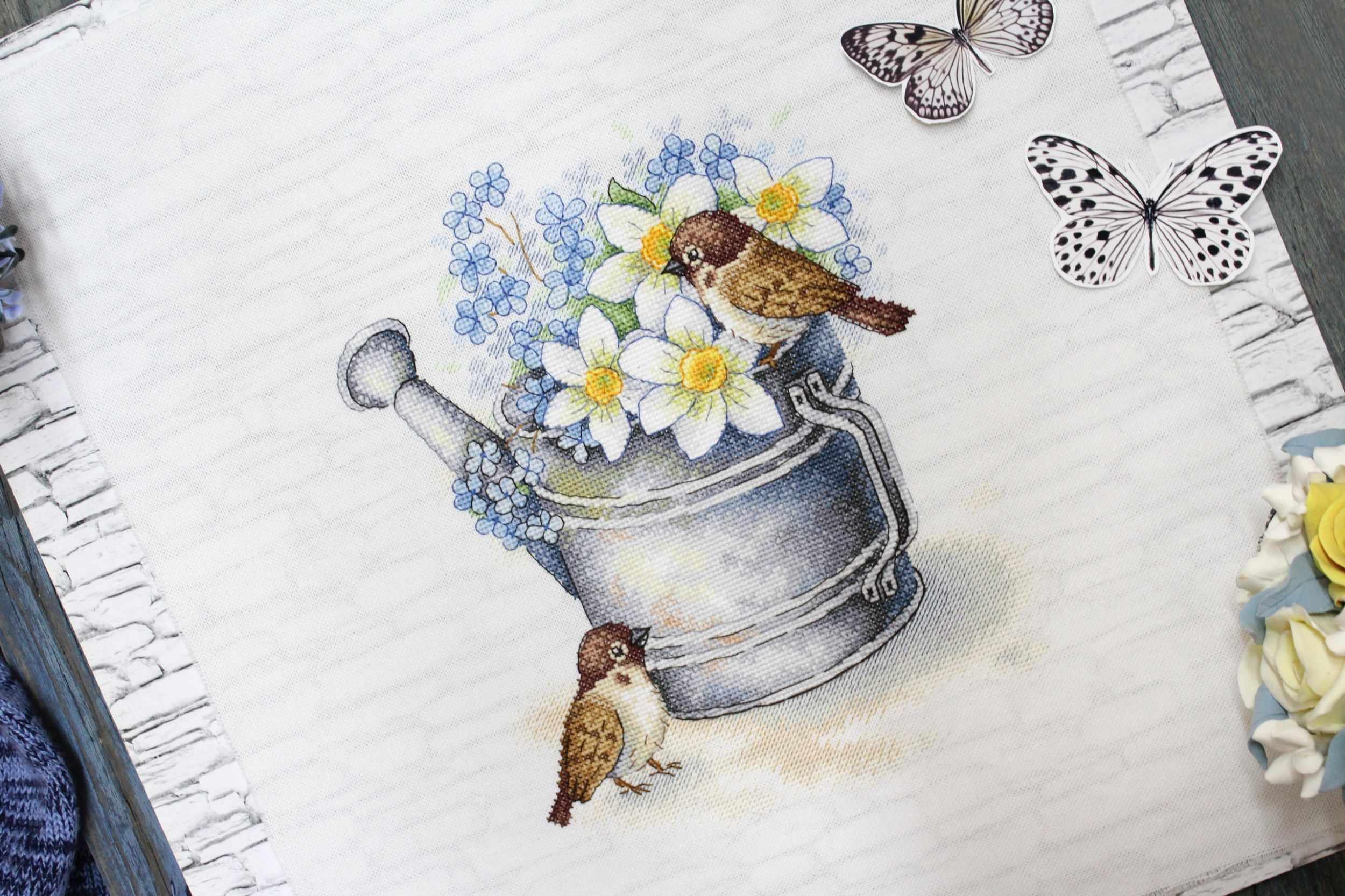 Daffodil Lovers SA-026 Cross-stitch kit featuring a watering can, white chamomiles, blue flowers, and a bullfinch on 27 count canvas.